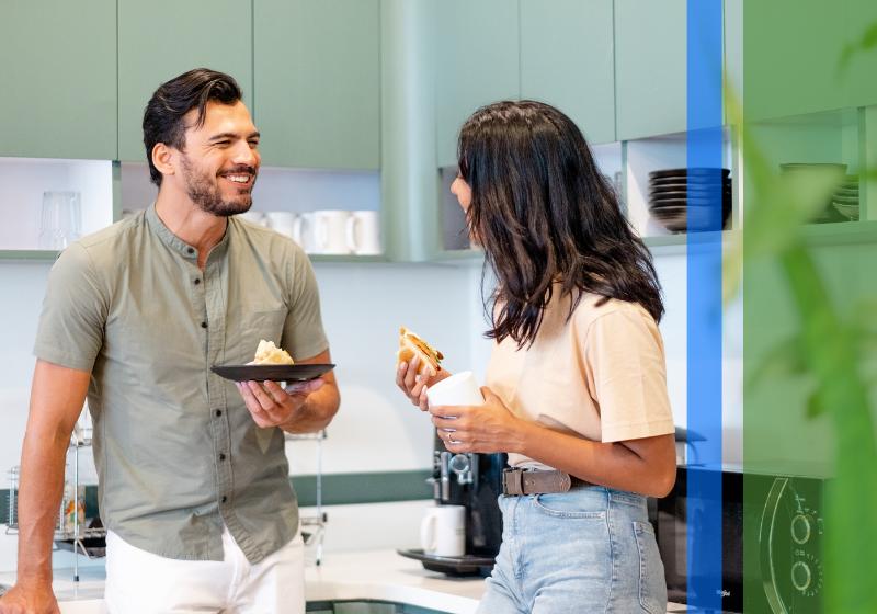 Two young adults smile and talk in a kitchen.