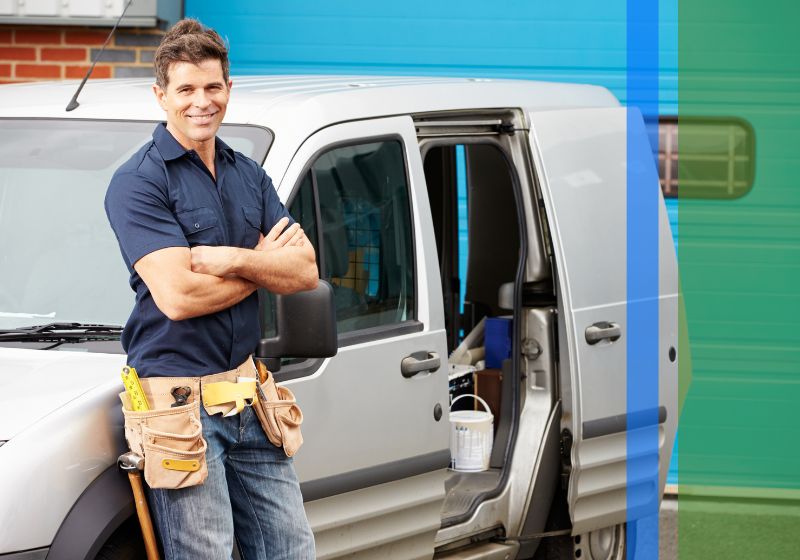 A professional, friendly plumber leaning against his work van.