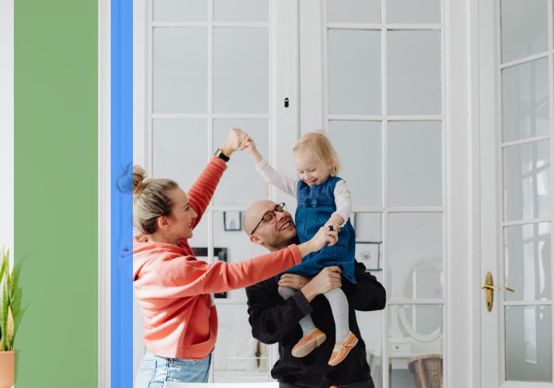 Two parents holding their young daughter and laughing in their home