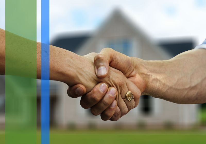A close up of a handshake in front of a house