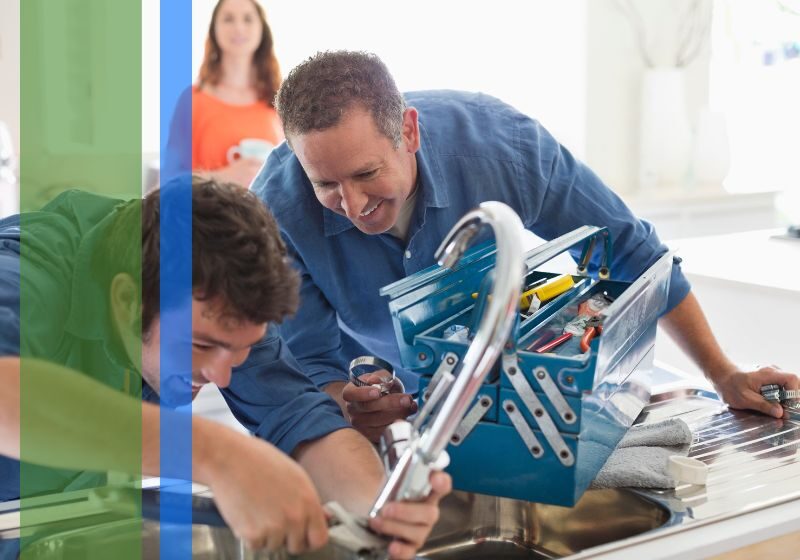 2 plumbers smiling working on a sink faucet