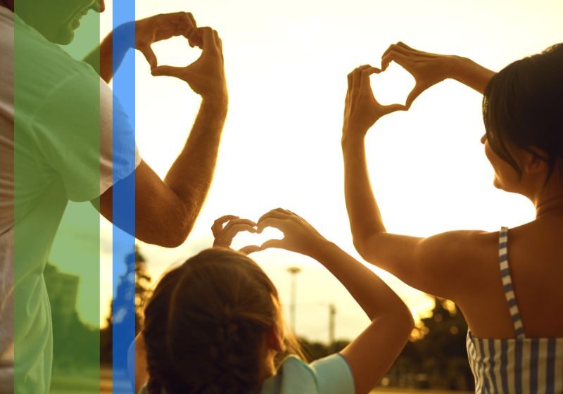 2 parents and their daughter making hearts with their hands towards the sunset